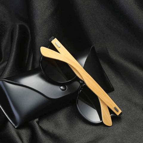 Óculos de sol Bamboo modelo dia a dia em ângulo diagonal traseiro em cima de um estojo preto na cor preto com lente verde escuro, disponível em: ethosloja.com.br