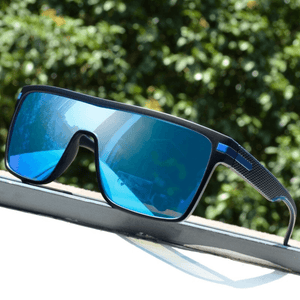 Óculos de sol Monte modelo dia a dia em ângulo diagonal com planta ao fundo na cor preto com azul, disponível em: ethosloja.com.br