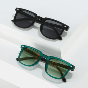 Dois óculos de sol Rivets modelo dia a dia em ângulo diagonal com as hastes fechadas na cor verde com leopardo e na cor preto, disponível em: ethosloja.com.br